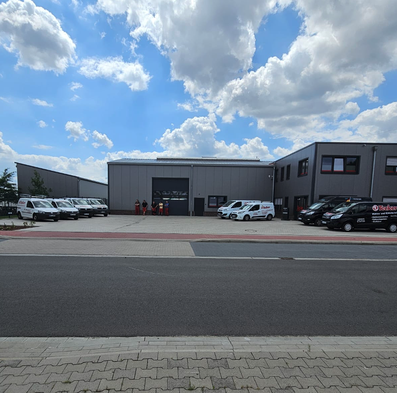 Aufnahme des Standorts von Tecker in Damme mit Bullis und Halle. Mitarbeiter stehen vor dem Tor